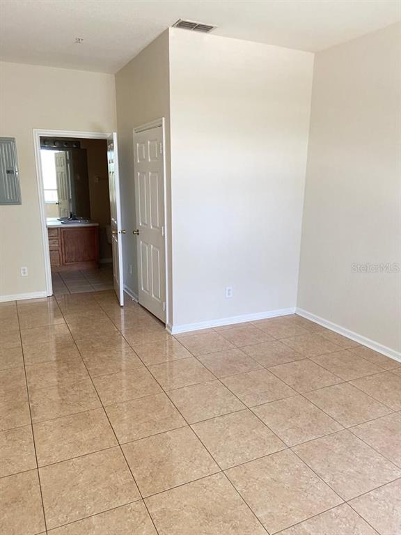 An empty room with beige tile flooring, a white door, and an open doorway to a bathroom — 6100 STEVENSON DRIVE UNIT 208, ORLANDO, FL