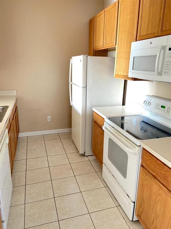 A kitchen features light-colored tile flooring, wood cabinets, and white appliances — 6100 STEVENSON DRIVE UNIT 208, ORLANDO, FL