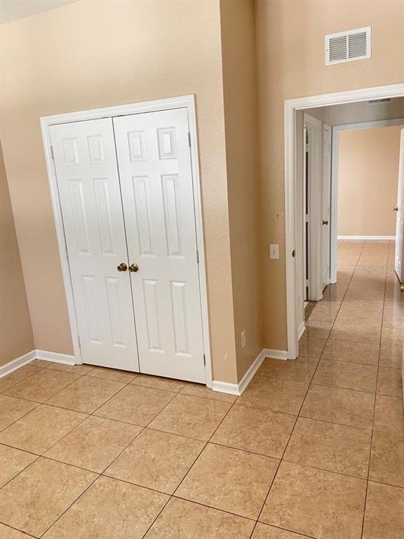 A room with beige walls, tiled floors, and white double closet doors leading to a hallway — 6100 STEVENSON DRIVE UNIT 208, ORLANDO, FL