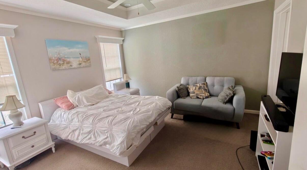 A bedroom features a white bed, a light blue loveseat, and a television on a stand — 7306 43rd Terrace N, Riviera Beach FL 33404, RIVIERA BEACH, FL