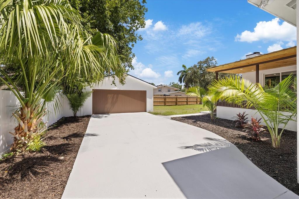 A concrete driveway leads to a detached garage next to a house with palm trees — 6403 ELLIOT DRIVE, TAMPA, FL