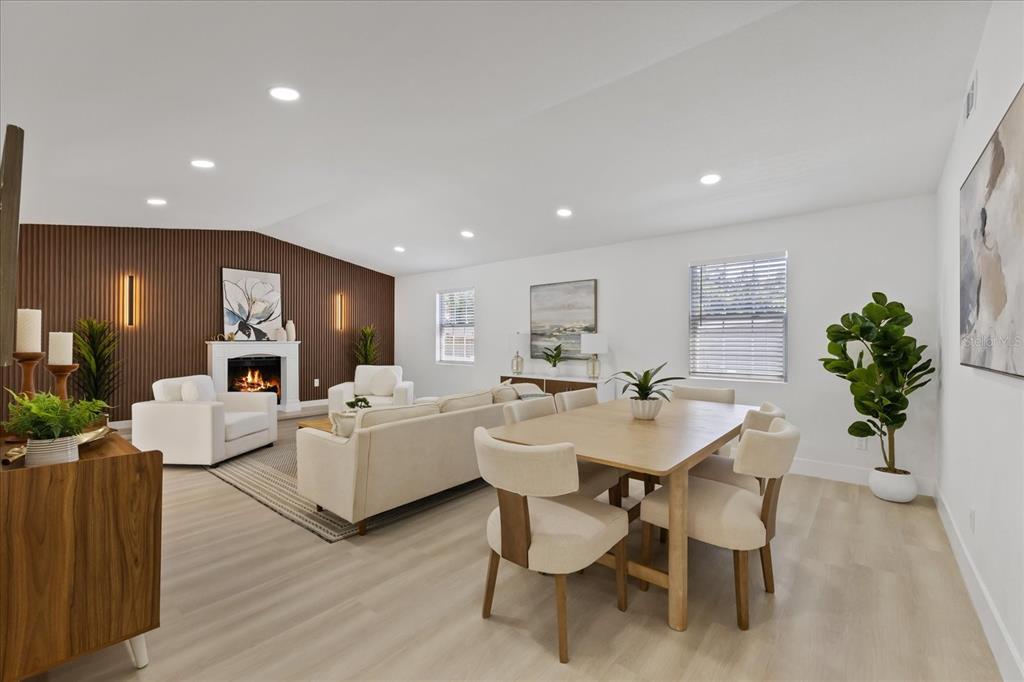 An open-concept living and dining area features light wood floors, a fireplace, and slatted walls — 6403 ELLIOT DRIVE, TAMPA, FL