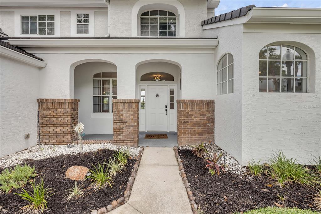 The exterior of a white stucco house features a brick-accented entryway and arched windows — 130 WIMBLEDON CIRCLE, LAKE MARY, FL