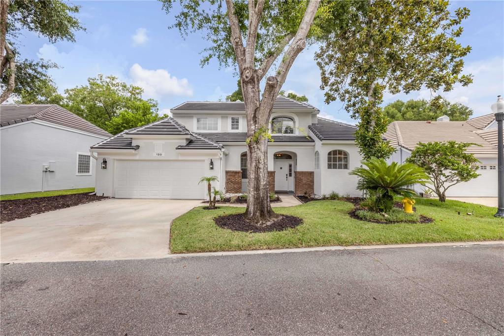 A two-story white house with a tile roof, a two-car garage, and mature trees — 130 WIMBLEDON CIRCLE, LAKE MARY, FL