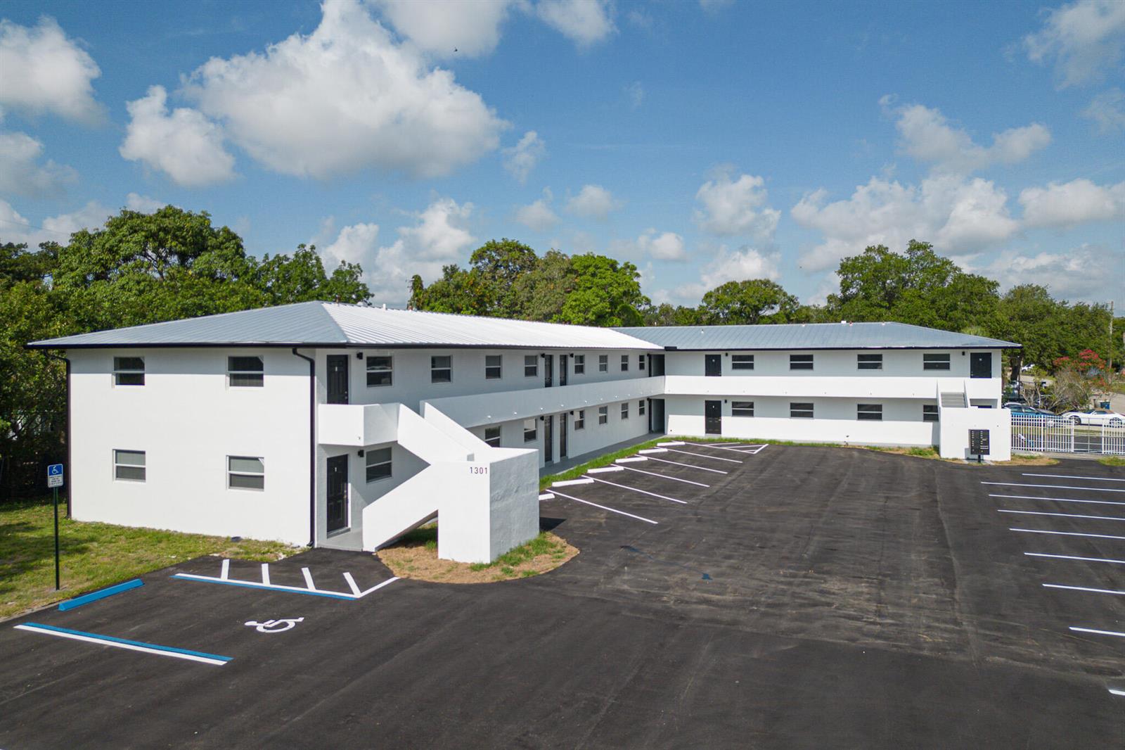 An exterior view of a two-story white apartment building with a large paved parking lot — 1301 Emerald Terrace # 3, Fort Pierce FL 34950, FORT PIERCE, FL