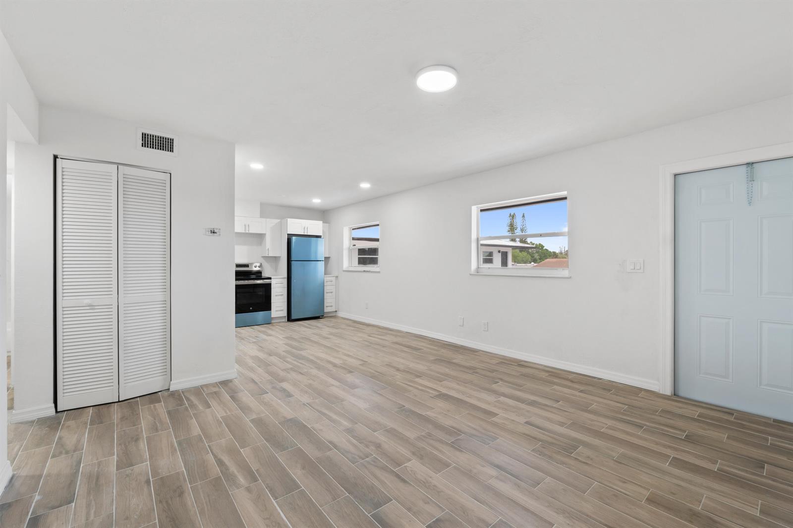 An open-concept room features light wood-look tile flooring, white walls, and an adjacent kitchen — 1301 Emerald Terrace # 3, Fort Pierce FL 34950, FORT PIERCE, FL
