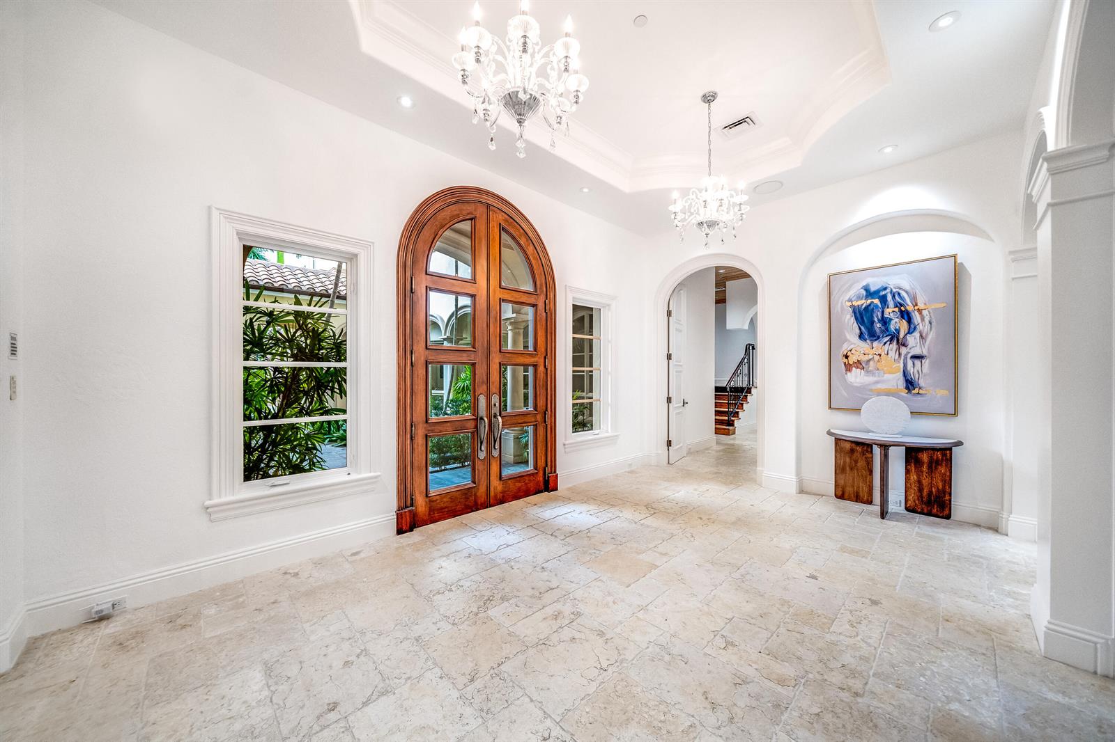 A bright foyer features stone tile flooring, two crystal chandeliers, and a large arched wooden door — 361 Mizner Lake Estates Drive, Boca Raton FL 33432, BOCA RATON, FL