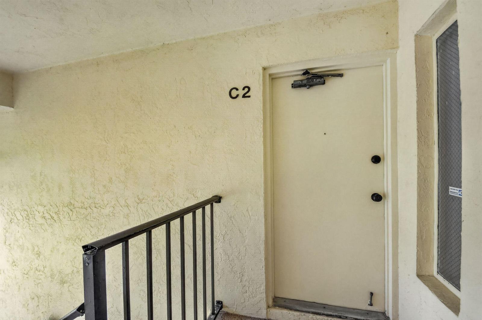 An exterior view of an apartment door labeled C2 with a black metal railing — 4991 Sable Pine Circle # C2, West Palm Beach FL 33417, WEST PALM BEACH, FL