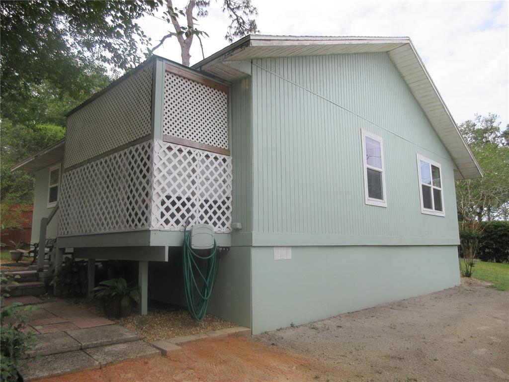 The exterior of a light green house features a lattice-enclosed porch and two windows — 5949 SE 164TH COURT, OCKLAWAHA, FL