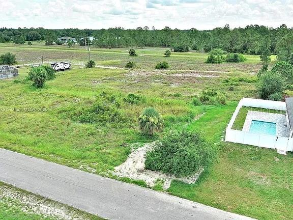 An aerial view shows a vacant grassy lot with a swimming pool and paved road — 1205 ROOSEVELT AVENUE, LEHIGH ACRES, FL