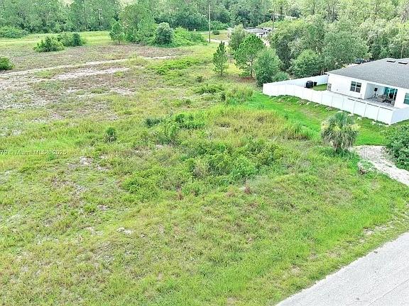 An aerial view shows a vacant, grassy lot next to a house with a white fence — 1205 ROOSEVELT AVENUE, LEHIGH ACRES, FL