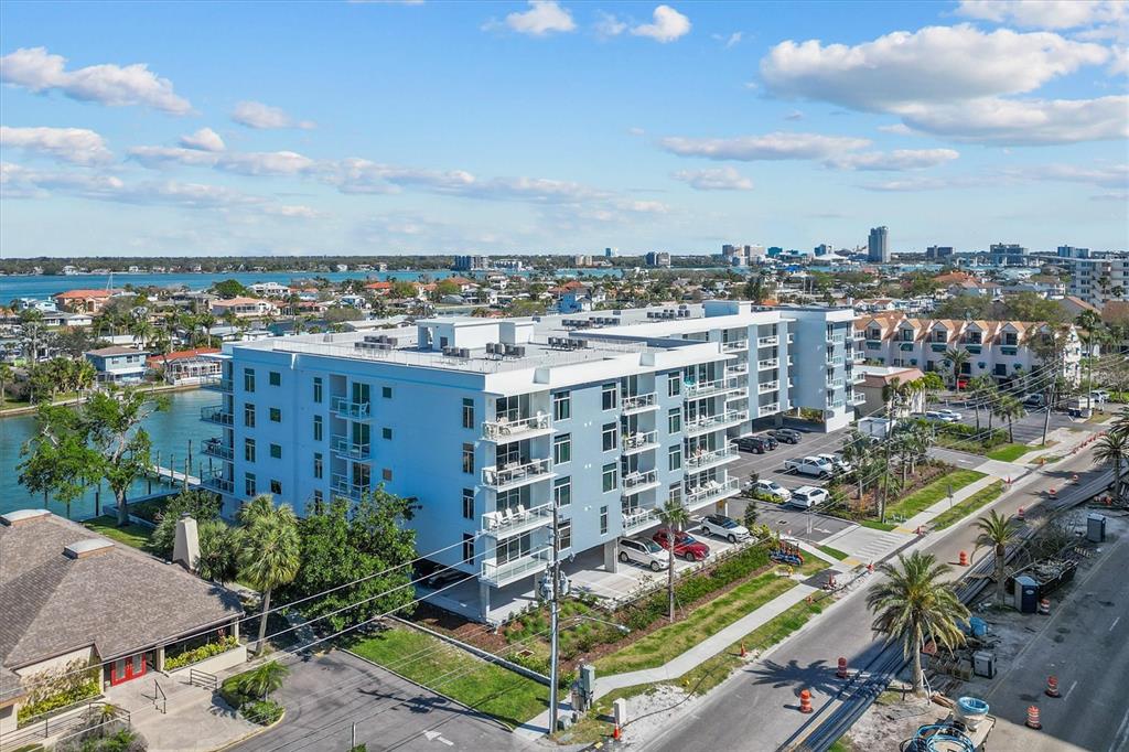 An aerial view shows a modern multi-story apartment building with balconies and a parking lot — 415 ISLAND WAY UNIT 311, CLEARWATER BEACH, FL