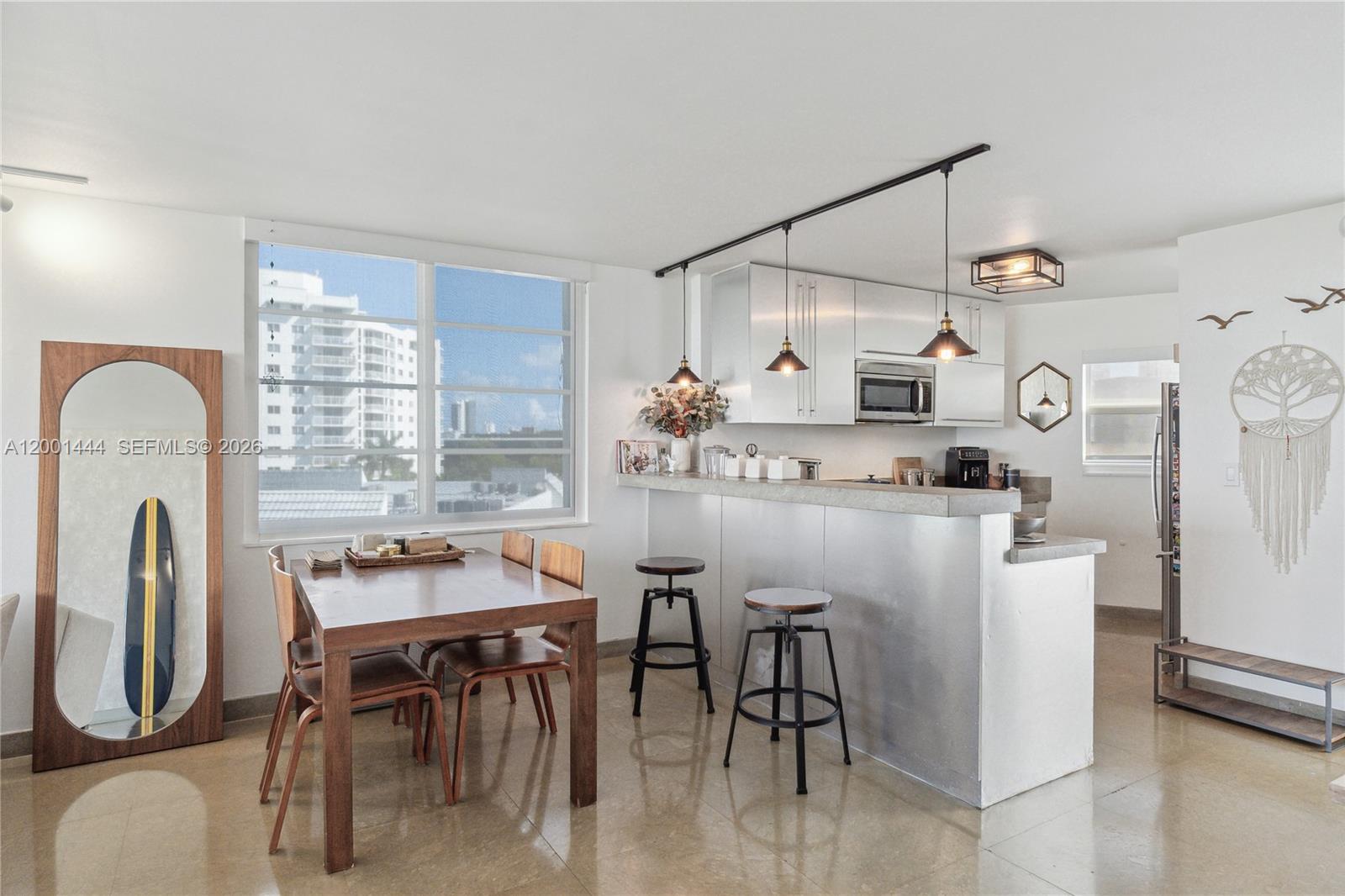 A kitchen and dining area features metallic cabinetry, a breakfast bar, and a large window — 1670 lincoln Ct, Miami Beach FL 33139, MIAMI BEACH, FL