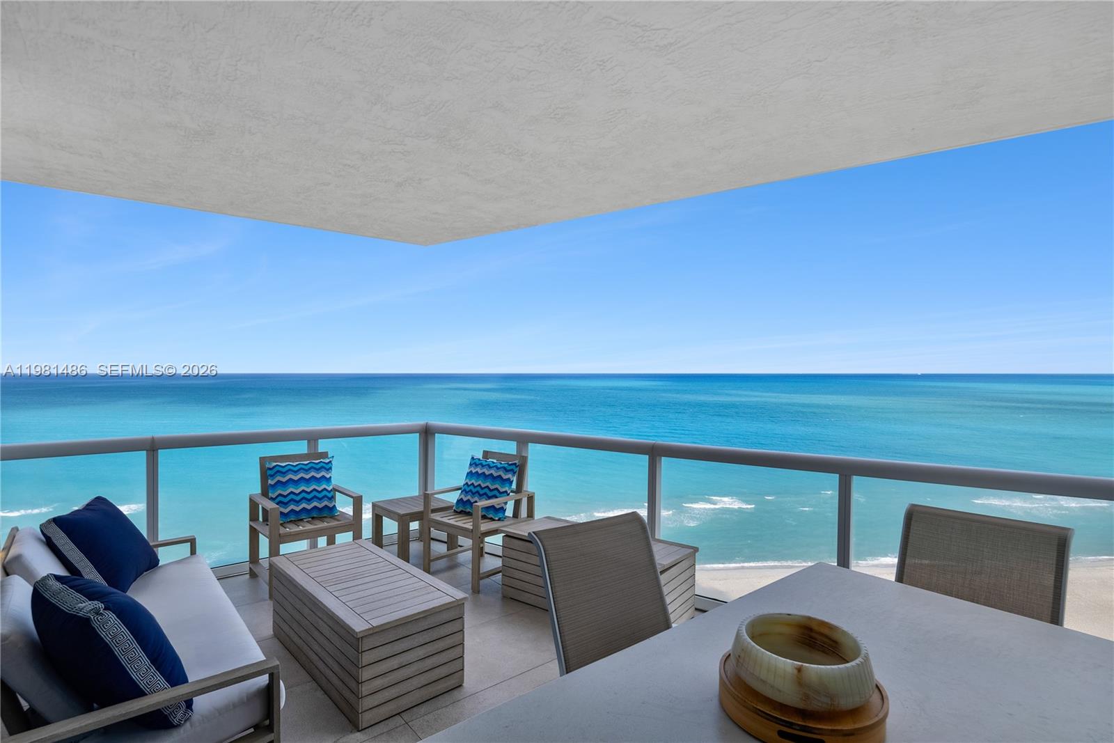 A balcony with outdoor furniture overlooks the ocean under a clear blue sky — 3801 Collins Ave # 1906, Miami Beach FL 33140, MIAMI BEACH, FL