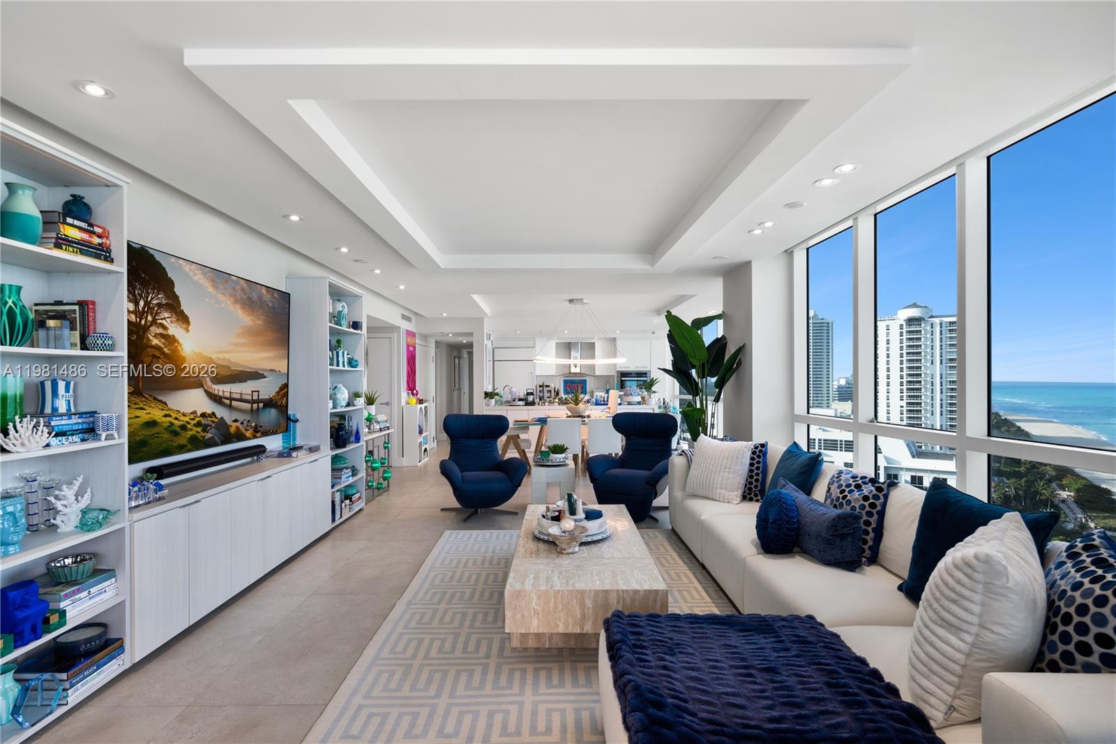 A modern living room features a large television, white cabinetry, blue armchairs, and ocean views — 3801 Collins Ave # 1906, Miami Beach FL 33140, MIAMI BEACH, FL