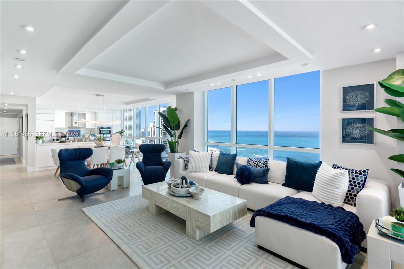 A modern living room features a white sectional, blue armchairs, and floor-to-ceiling ocean views — 3801 Collins Ave # 1906, Miami Beach FL 33140, MIAMI BEACH, FL