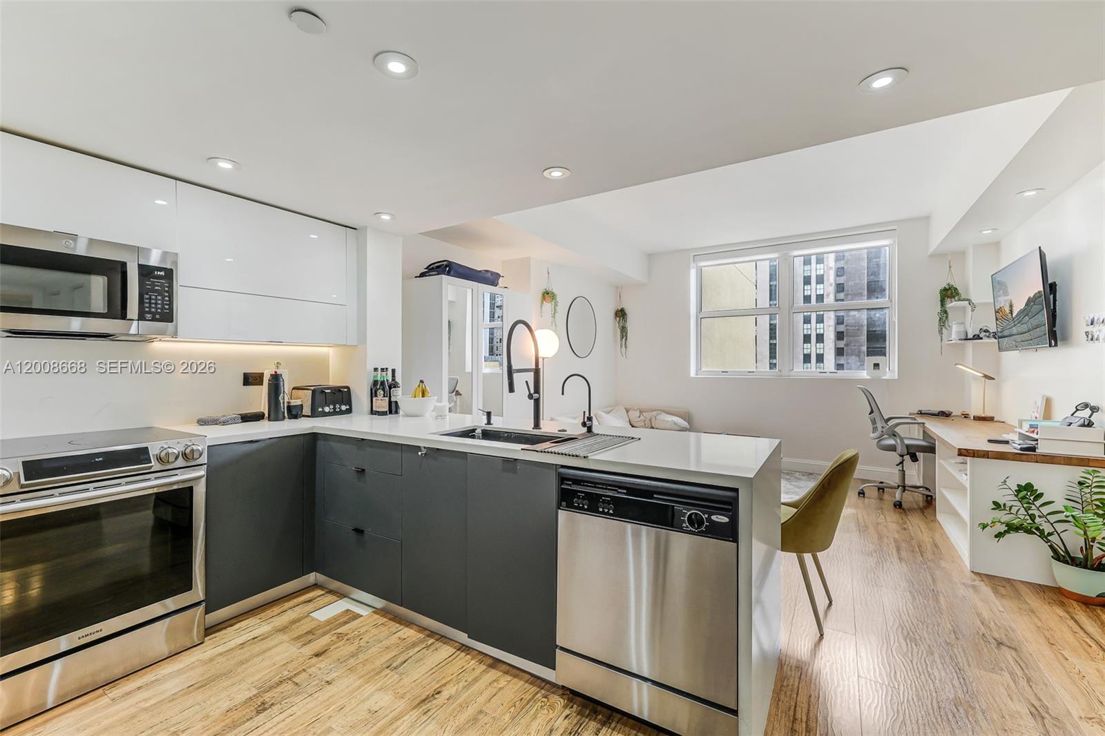 A modern kitchen with dark grey cabinets and stainless steel appliances opens to a workspace — 111 E Flagler St # 708, Miami FL 33131, MIAMI, FL
