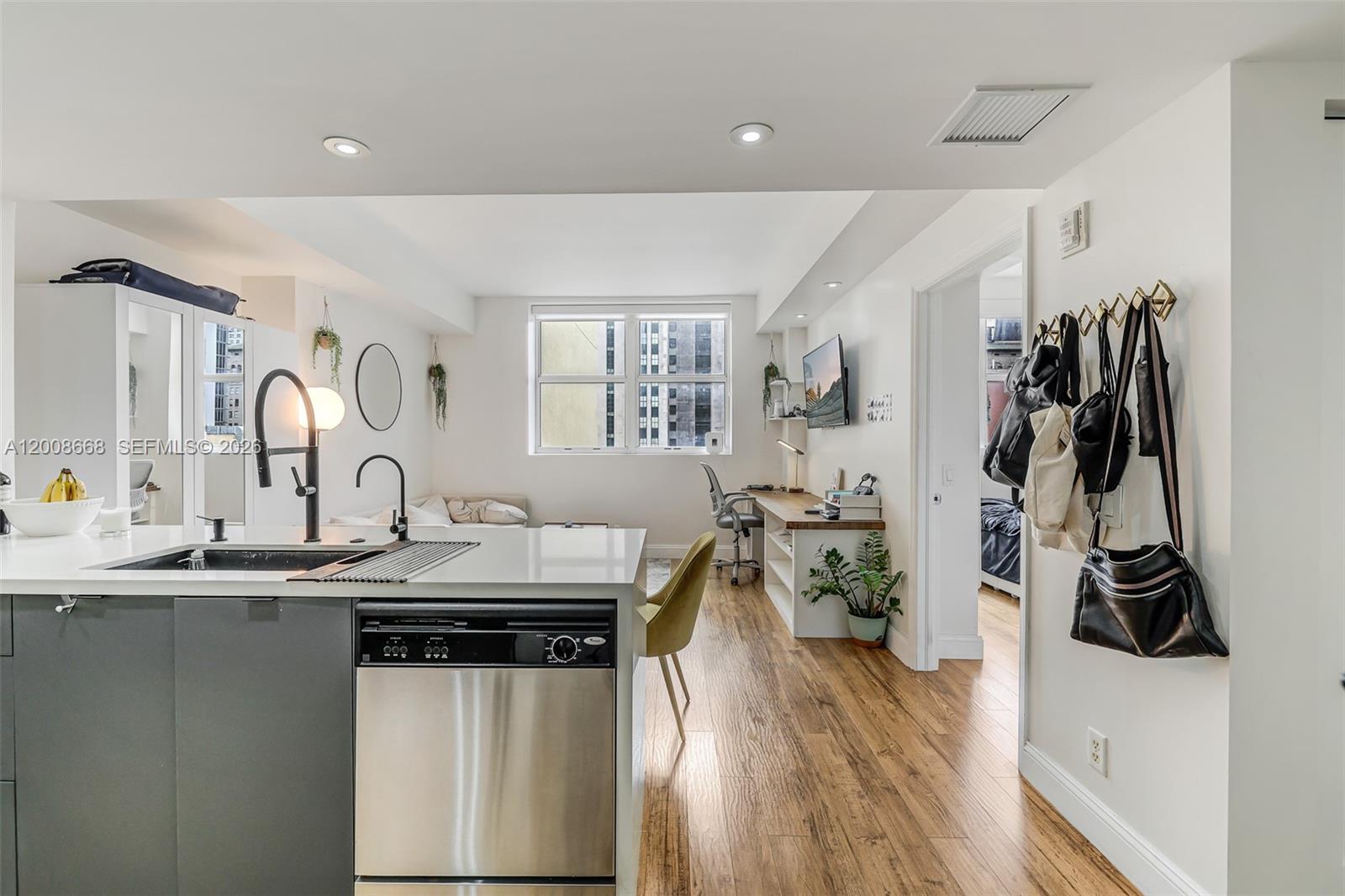 A modern studio apartment features a kitchen island, hardwood floors, and a built-in desk area — 111 E Flagler St # 708, Miami FL 33131, MIAMI, FL