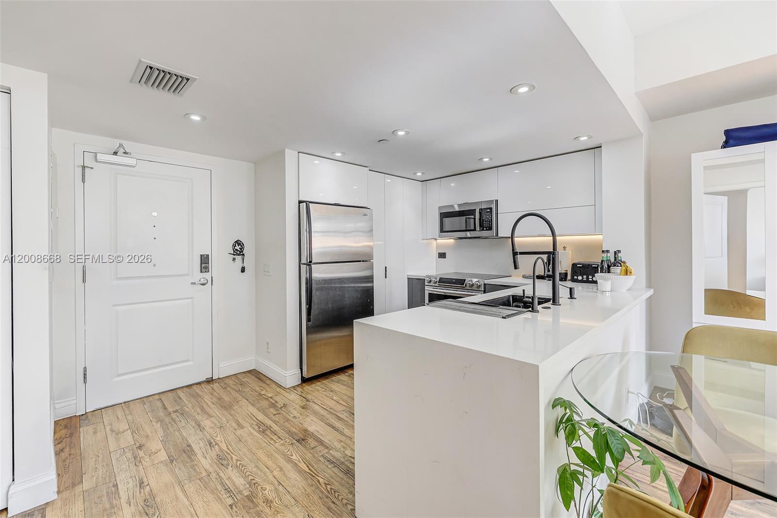 A modern kitchen features white cabinetry, stainless steel appliances, and a white quartz island — 111 E Flagler St # 708, Miami FL 33131, MIAMI, FL