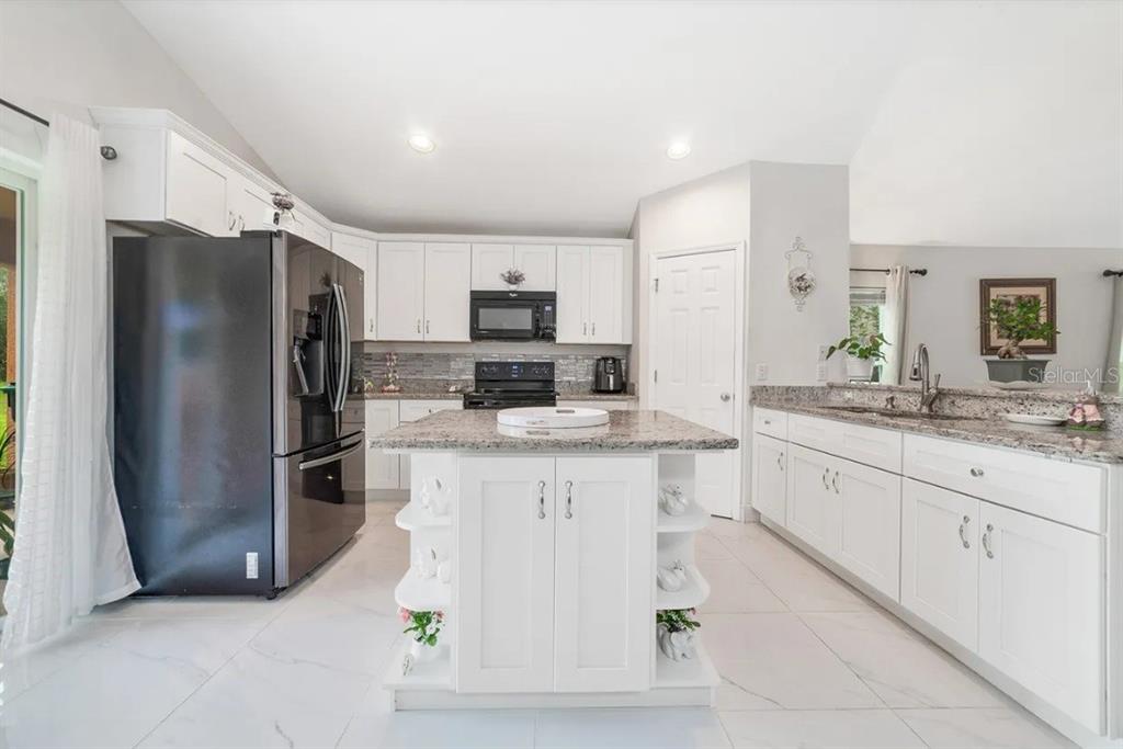 A kitchen features white cabinetry, a granite-topped island, black appliances, and light tile flooring — 15649 CARINA DRIVE, ORLANDO, FL