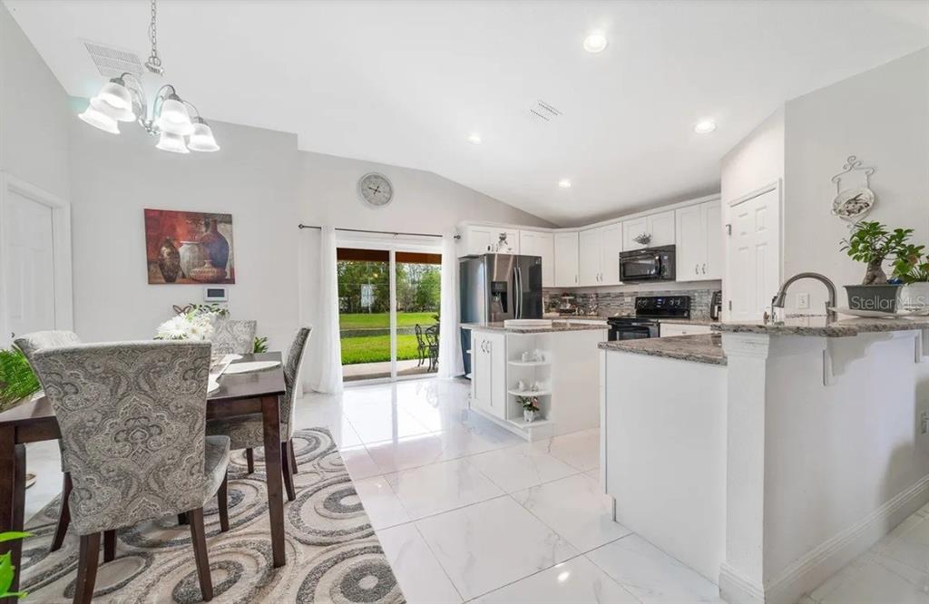 A bright kitchen and dining area with white cabinets, granite countertops, and white tile flooring — 15649 CARINA DRIVE, ORLANDO, FL