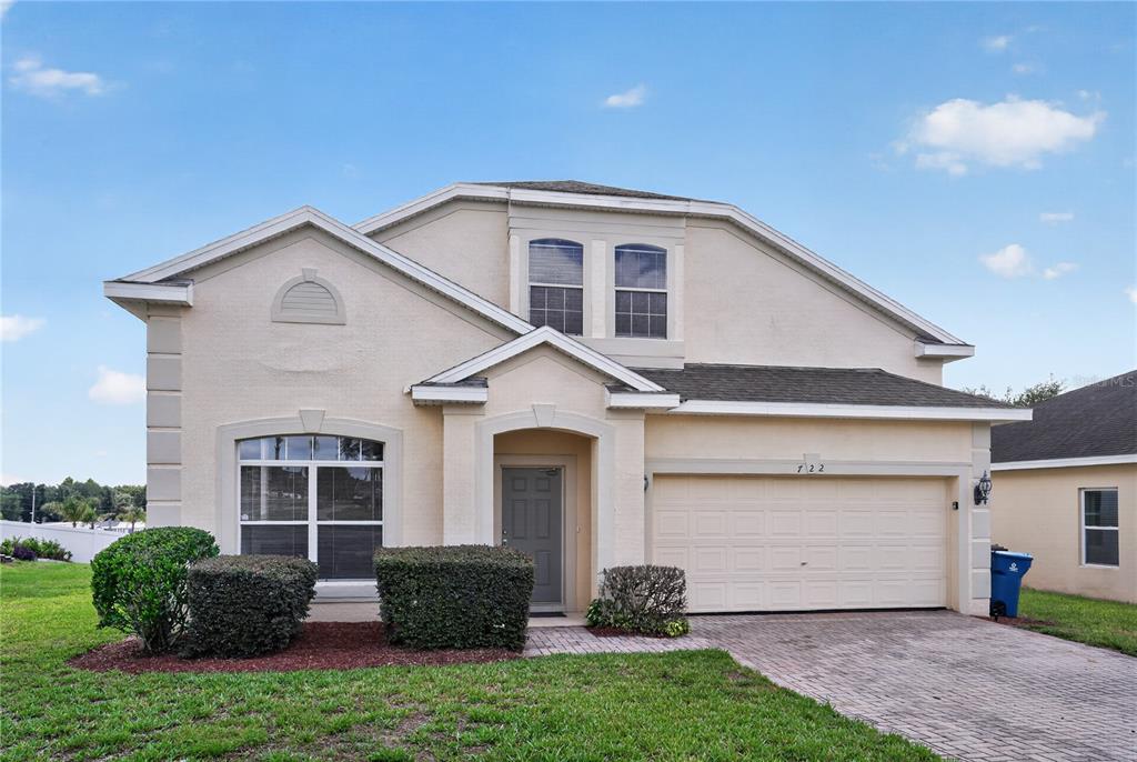 A two-story suburban home with a beige stucco exterior, a garage, and a paved driveway — 722 CADIZ LOOP, DAVENPORT, FL