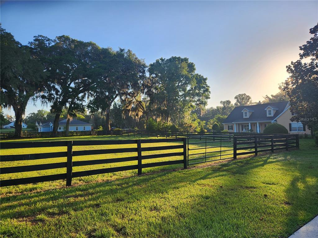 A black wooden fence encloses a grassy pasture in front of a house and trees — 9041 SW 14TH AVENUE, OCALA, FL