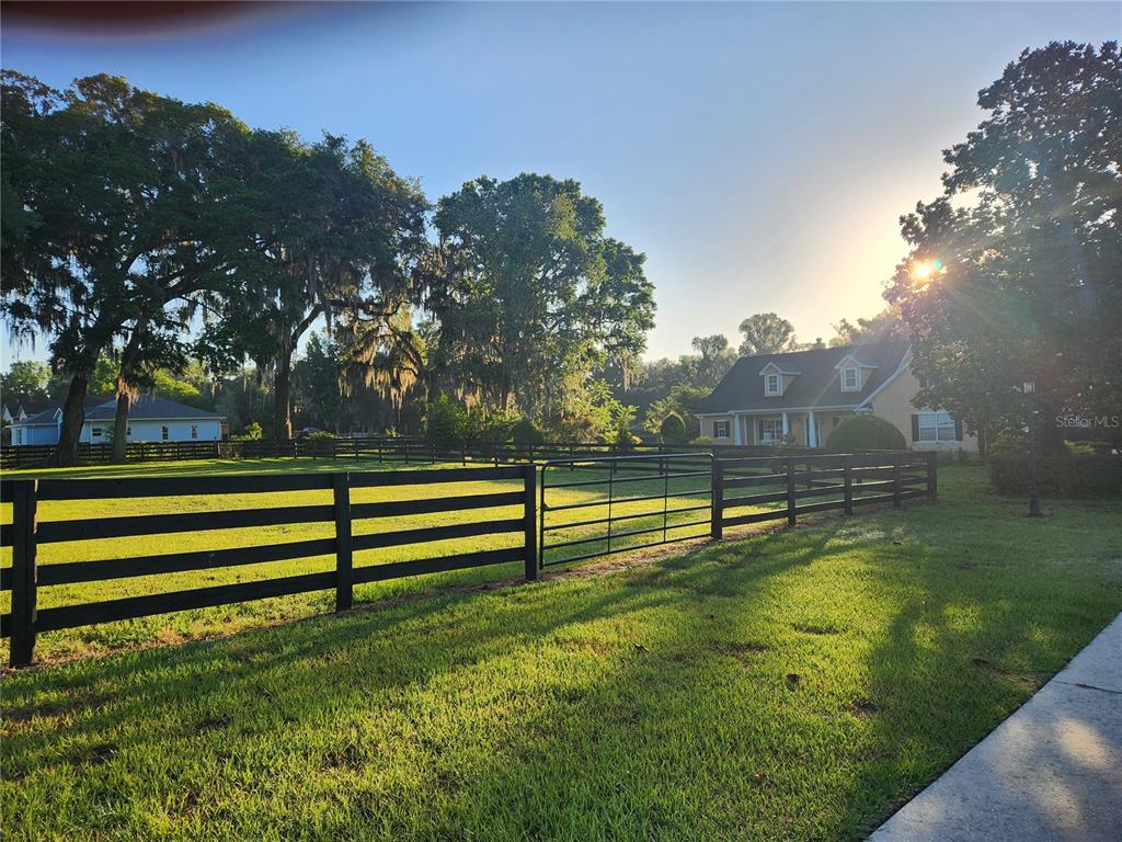 A black wooden fence encloses a grassy yard in front of a yellow house — 9041 SW 14TH AVENUE, OCALA, FL