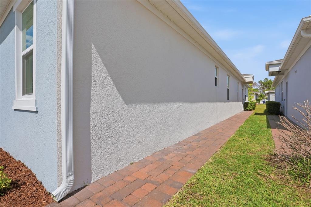 A paved walkway runs along the side of a house with light-colored stucco walls — 1841 OVERCUP AVENUE, ST CLOUD, FL