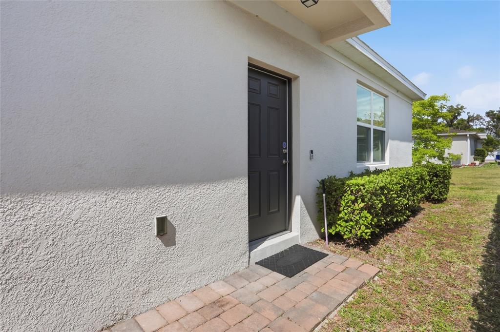 A dark gray door with a brick walkway and a hedge sits on the exterior — 1841 OVERCUP AVENUE, ST CLOUD, FL