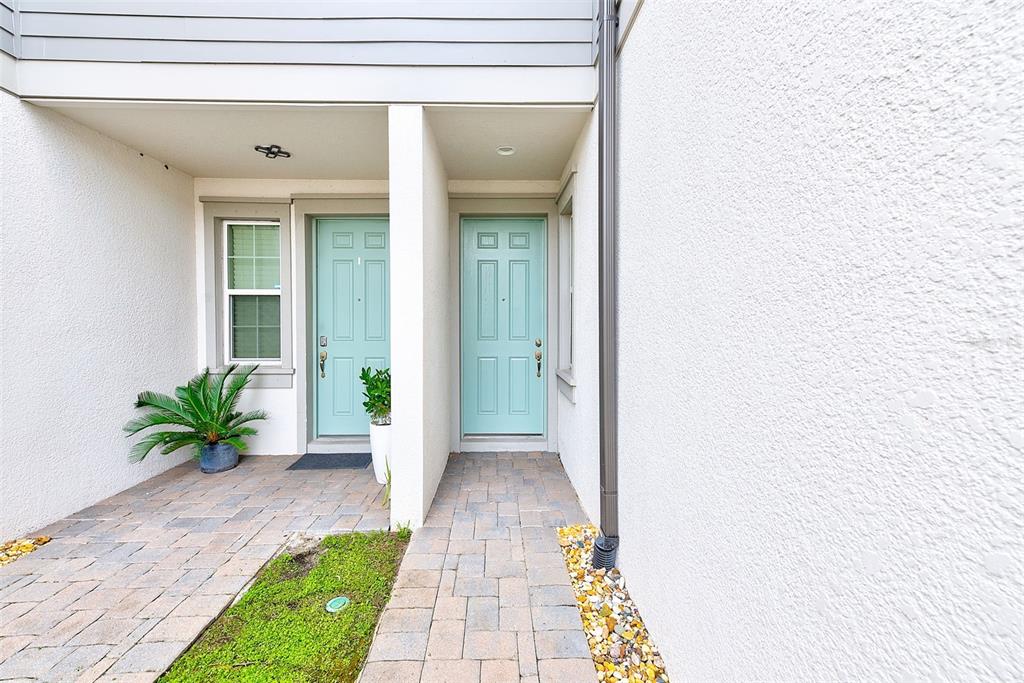 Two light blue front doors are set in a white stucco entryway with paver walkways — 2441 FOGGY CREEK CIRCLE, CLEARWATER, FL
