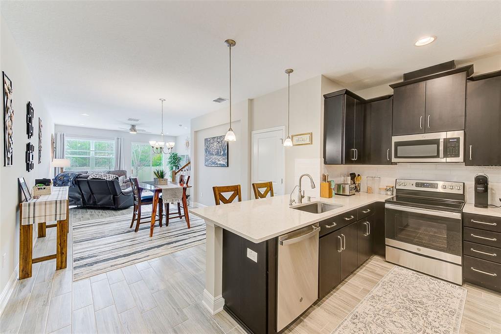 A kitchen with dark cabinets and a quartz island overlooks a dining and living area — 2441 FOGGY CREEK CIRCLE, CLEARWATER, FL