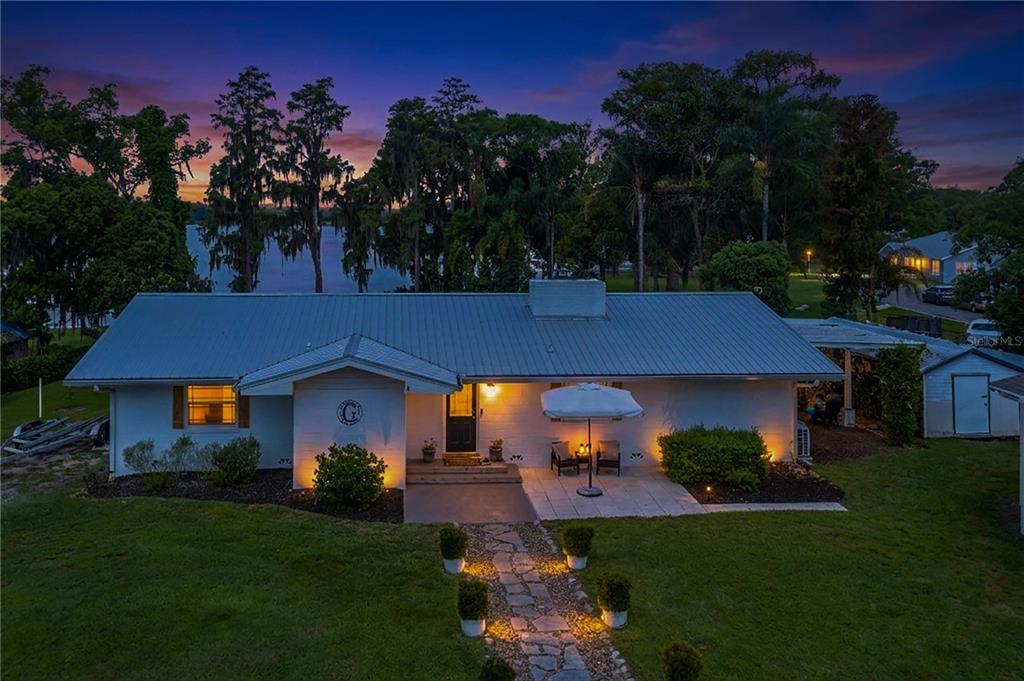 A single-story house with a metal roof and stone walkway sits near a lake — 775 S BUENA VISTA DRIVE, LAKE ALFRED, FL