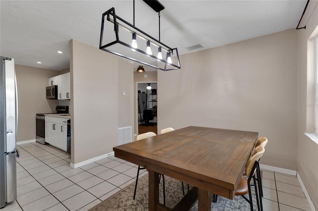 A dining area features a wooden table, a modern rectangular pendant light, and tiled floors — 217 ROSE STREET, AUBURNDALE, FL
