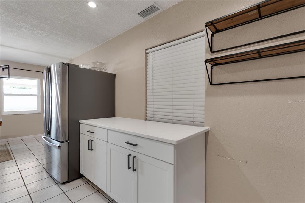 A kitchen features white cabinets, a stainless steel refrigerator, and two wall-mounted open shelves — 217 ROSE STREET, AUBURNDALE, FL