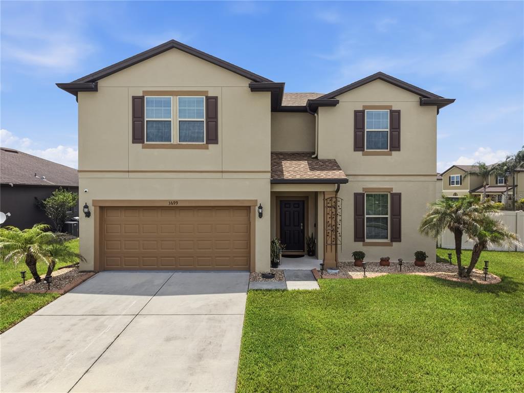 A two-story beige house with a brown garage door, shutters, and a front lawn — 3699 MOCA DRIVE, ST CLOUD, FL