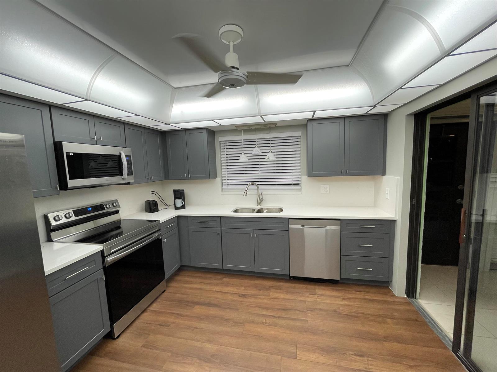 A kitchen features gray shaker cabinets, stainless steel appliances, white countertops, and wood-look flooring — 4450 Nutmeg Tree Lane # B, Boynton Beach FL 33436, BOYNTON BEACH, FL