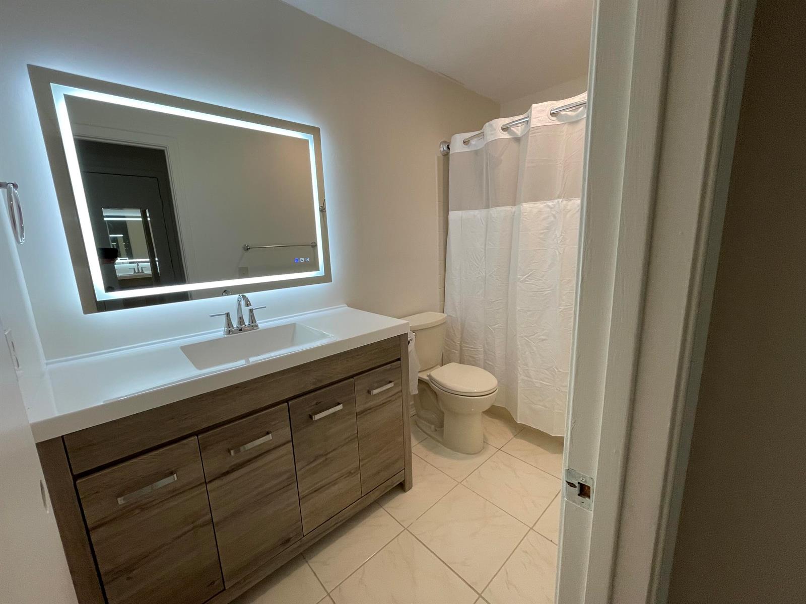 A bathroom features a wood vanity, a lighted mirror, a toilet, and a shower curtain — 4450 Nutmeg Tree Lane # B, Boynton Beach FL 33436, BOYNTON BEACH, FL