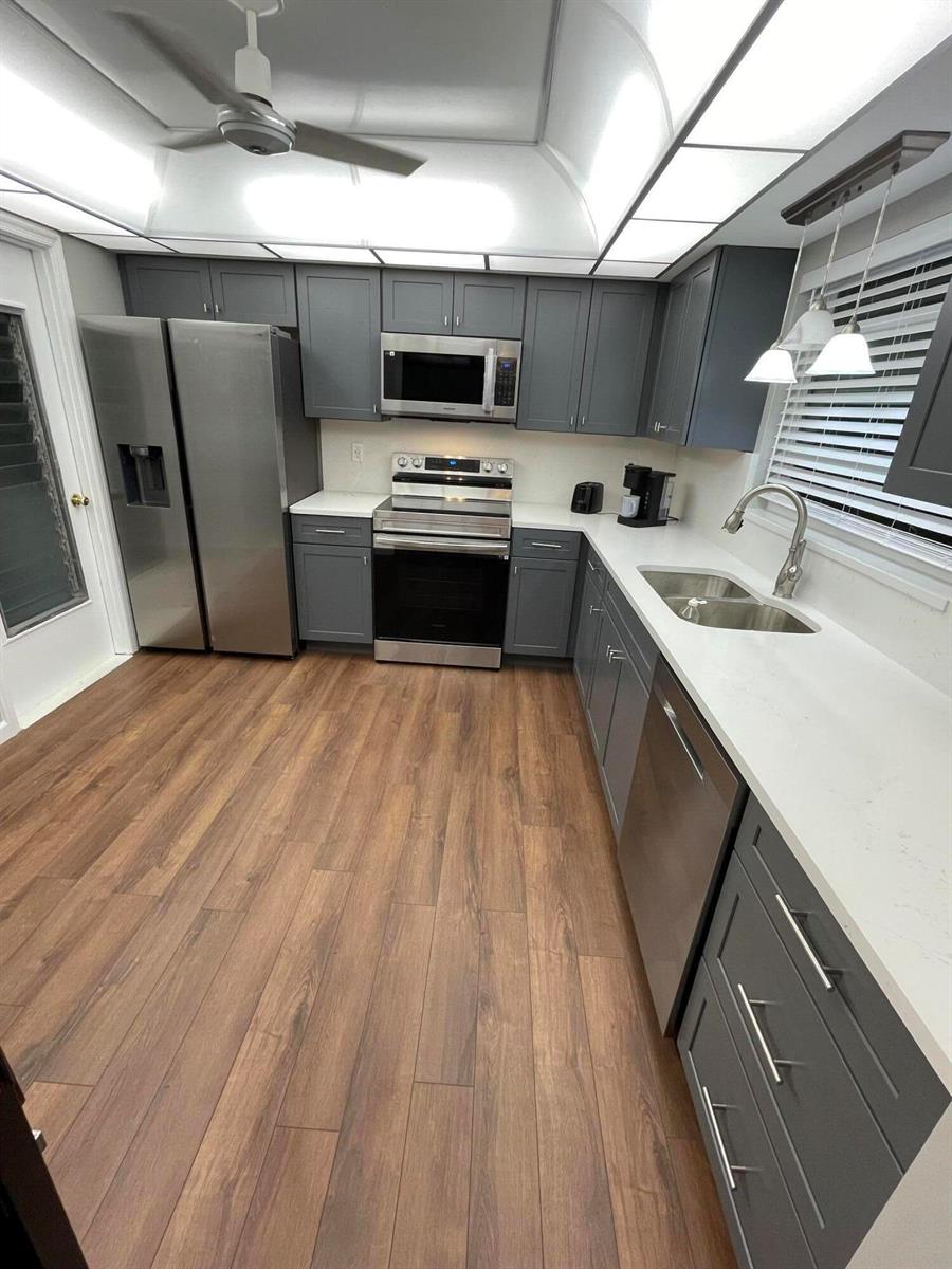 A kitchen features gray cabinets, stainless steel appliances, white countertops, and wood-look flooring — 4450 Nutmeg Tree Lane # B, Boynton Beach FL 33436, BOYNTON BEACH, FL