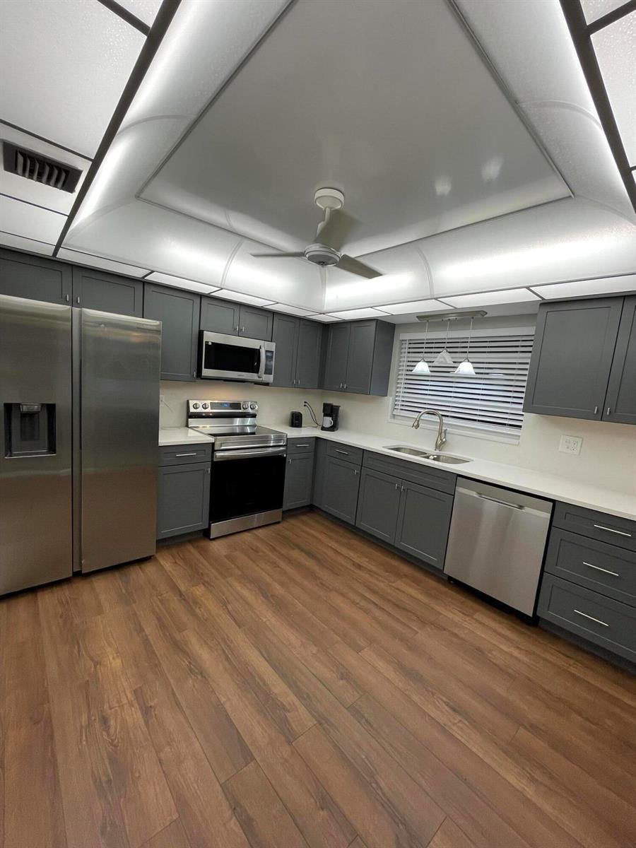 A kitchen features dark grey cabinets, stainless steel appliances, white countertops, and wood-look flooring — 4450 Nutmeg Tree Lane # B, Boynton Beach FL 33436, BOYNTON BEACH, FL