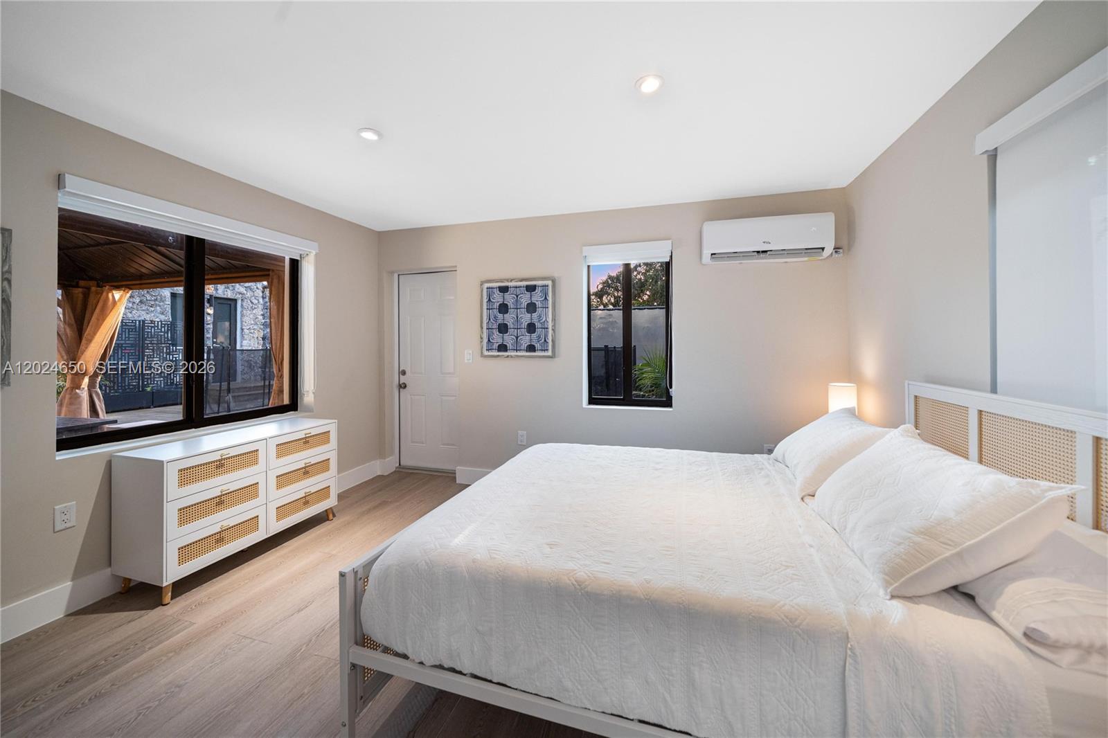 A bedroom features a white bed, a cane-accented dresser, and a wall-mounted air conditioning unit — 1663 SW 13th St, Miami FL 33145, MIAMI, FL