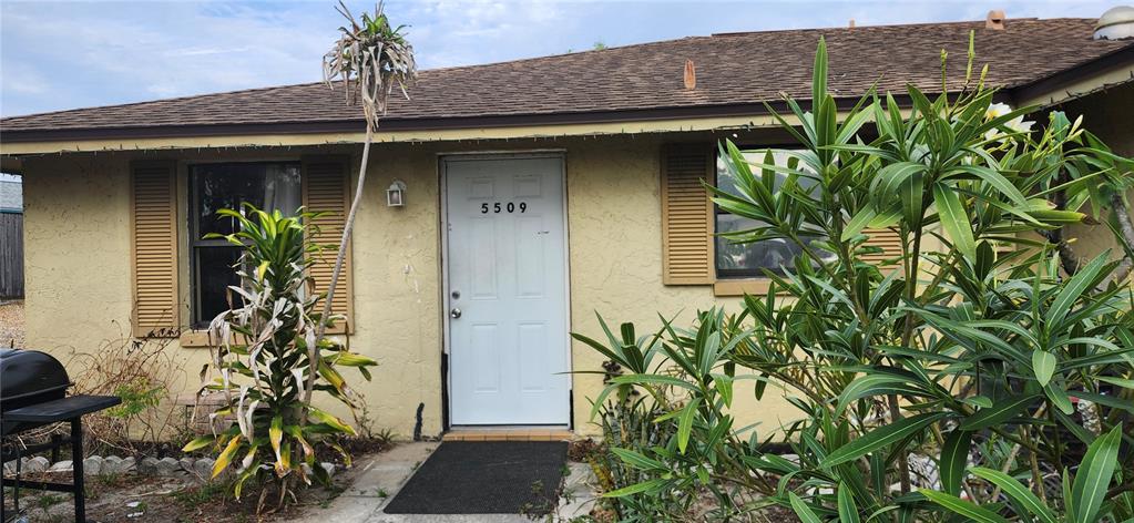 The exterior of a single-story house features a white front door and surrounding landscaping — 5509 RIDDLE ROAD, HOLIDAY, FL