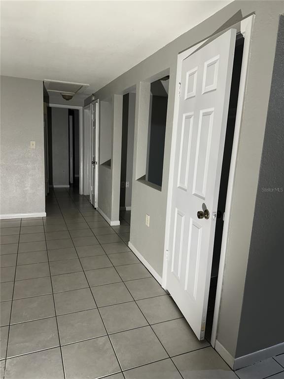 A hallway with light gray walls and tiled flooring leads to several doorways and openings — 5509 RIDDLE ROAD, HOLIDAY, FL