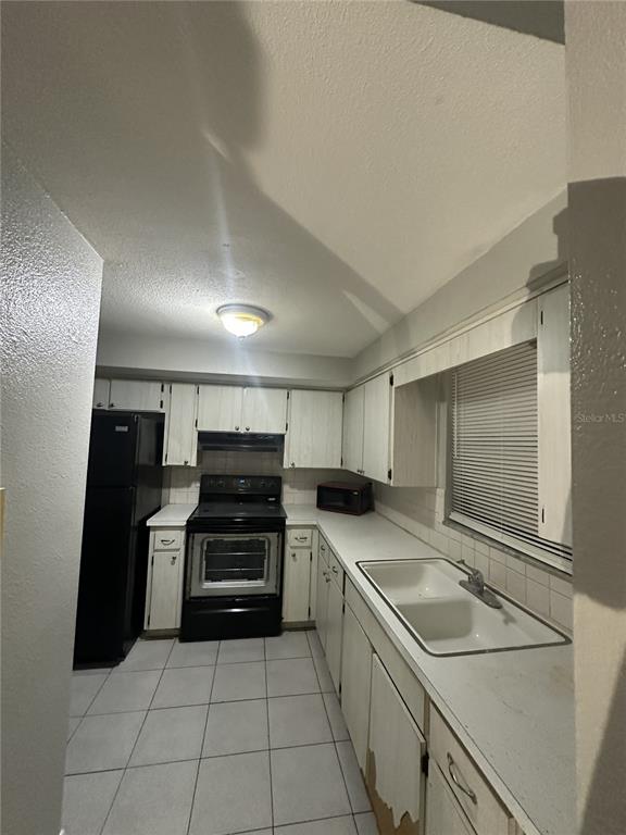 A kitchen with white cabinets, black appliances, a double sink, and light-colored floor tiles — 5509 RIDDLE ROAD, HOLIDAY, FL