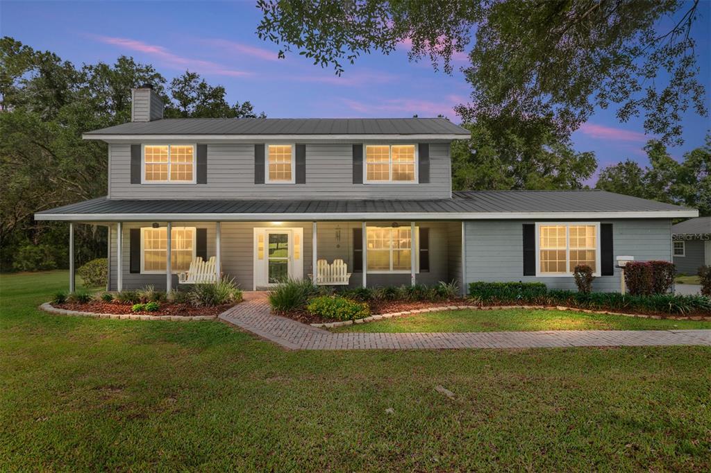 A two-story gray house with a metal roof and a brick walkway at dusk — 12014 NW 136TH STREET, ALACHUA, FL
