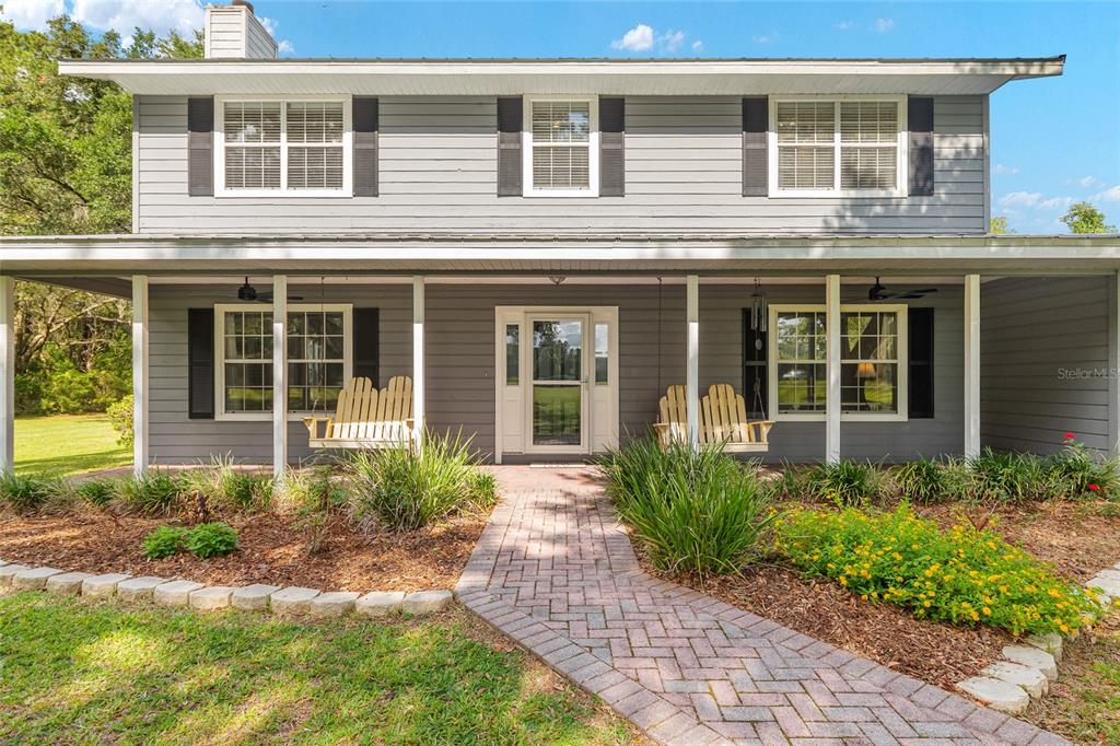 A two-story gray house features a covered front porch with two wooden swings — 12014 NW 136TH STREET, ALACHUA, FL