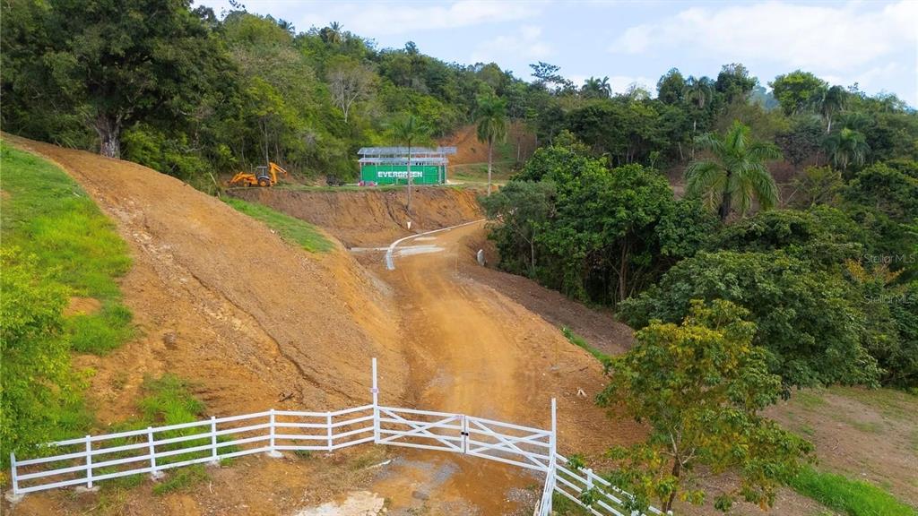 An aerial view shows a dirt road leading to a green shipping container on a hillside — CARR 827 KM 5.0, INTERIOR, BO. ORTIZ, LOT 1 & 2, TOA ALTA, PR