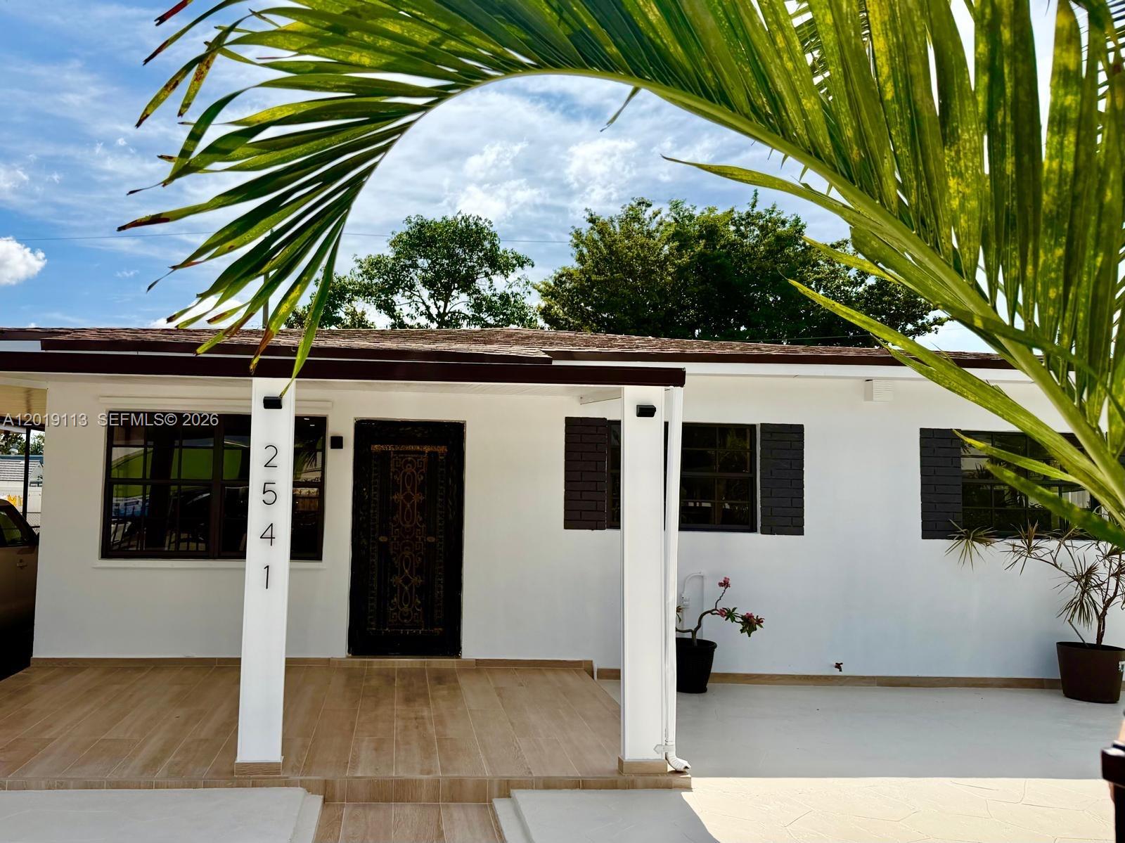 A white house exterior features a covered porch, dark shutters, and a decorative front door — 2541 W 10th Ave, Hialeah FL 33010, HIALEAH, FL