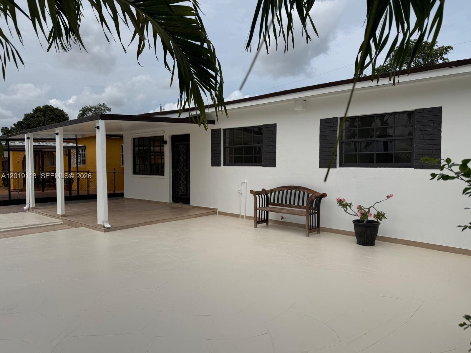 A white house exterior features a covered patio, a wooden bench, and dark window shutters — 2541 W 10th Ave, Hialeah FL 33010, HIALEAH, FL