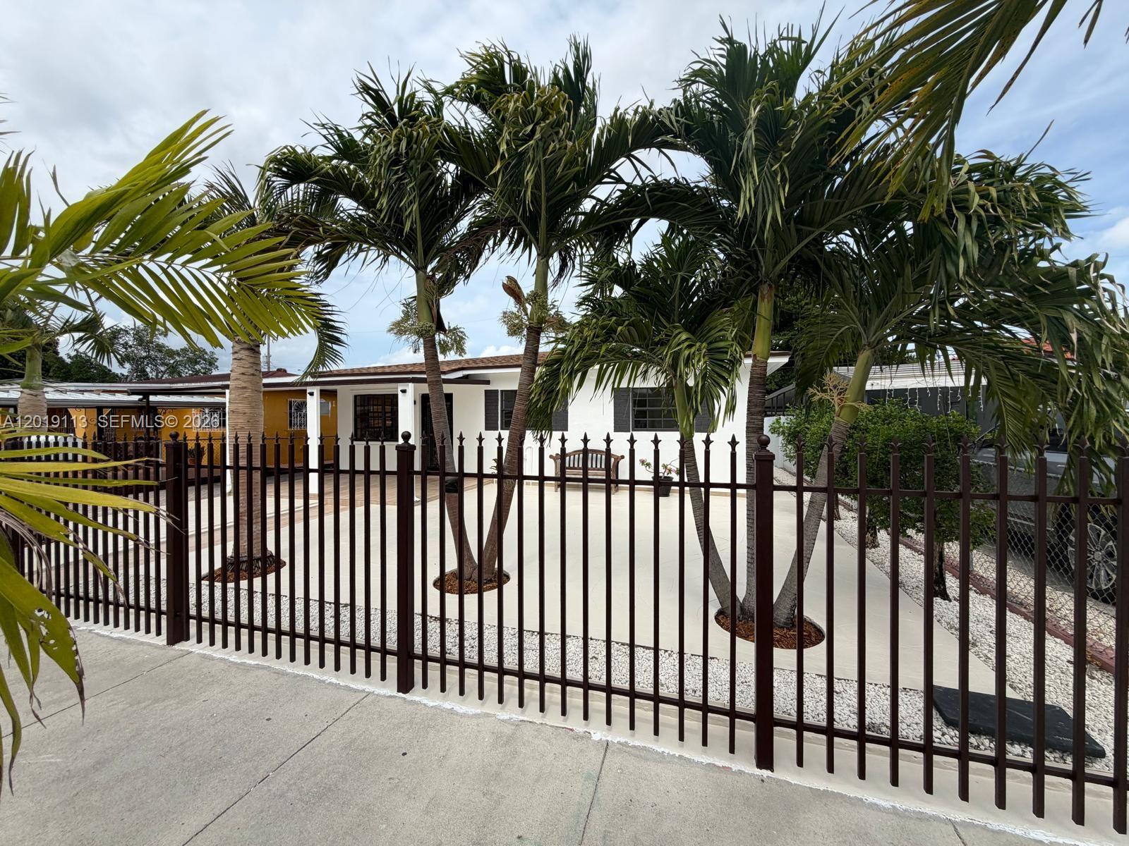 A white single-story house with palm trees behind a brown metal fence — 2541 W 10th Ave, Hialeah FL 33010, HIALEAH, FL